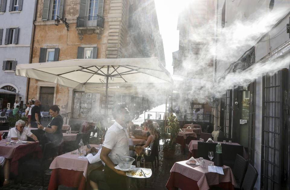 FILE - In this Friday, July 31, 2020 file photo, a fan sprays water mist as customers sit outside a cafe in downtown Rome during a heat wave with temperatures over 34 Celsius (104 Fahrenheit). (AP Photo/Riccardo De Luca)