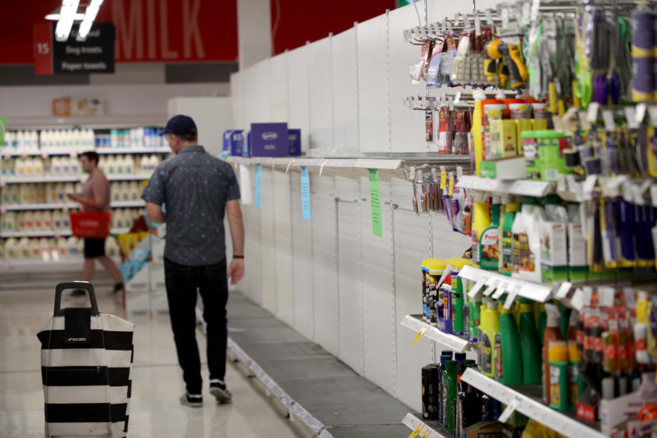 Two Coles shoppers are walking inside an Adelaide store where the toilet paper aisle is empty.