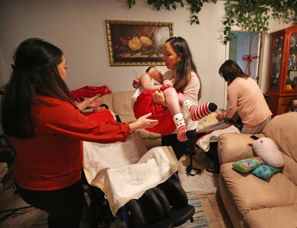 Justin Nguyen, 24, is carried by his sister Jennifer Pham to his wheelchair as their older sister, Jessica Pham, reaches out to assist her. Their mother, Julie Nguyen, works on Justin’s equipment in the background. Justin, who was severely injured during birth, is cared for around the clock by his family in their Jacksonville home. 