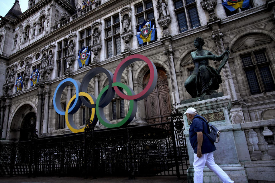 FILE - A man walks past the Olympic rings in front of the Paris City Hall one year until the Paris 2024 Olympic Games opening ceremony, Wednesday, July 26, 2023. Officials spent more than two hours explaining the security, traffic and other arrangements that will be in place and took questions. Paris officials, Games organizers and government ministries are in the midst of concerted campaigns to explain to Parisians how the July 26-Aug.11 Summer Olympics and Paralympics that follow will impact their lives and how they can adapt. (AP Photo/Christophe Ena, File)