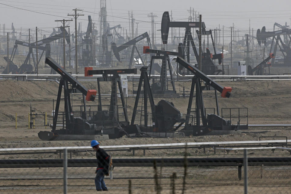 FILE - In this Jan. 16, 2015, file photo, a person walks past pump jacks operating at the Kern River Oil Field in Bakersfield, Calif. California's oil rich Kern County is voting on a revised plan that could permit tens of thousands of oil and gas wells in the next two decades. The plan had to be rewritten after environmental groups sued and a state appeals court found the county's permit system could threaten the region's air and water. (AP Photo/Jae C. Hong, File)