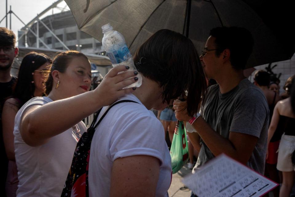 An Eras Tour concertgoer on 18 November helps another attendee cool down by placing a water bottle against the back of their neck (Terico Teixeira/AFP via Getty Images)