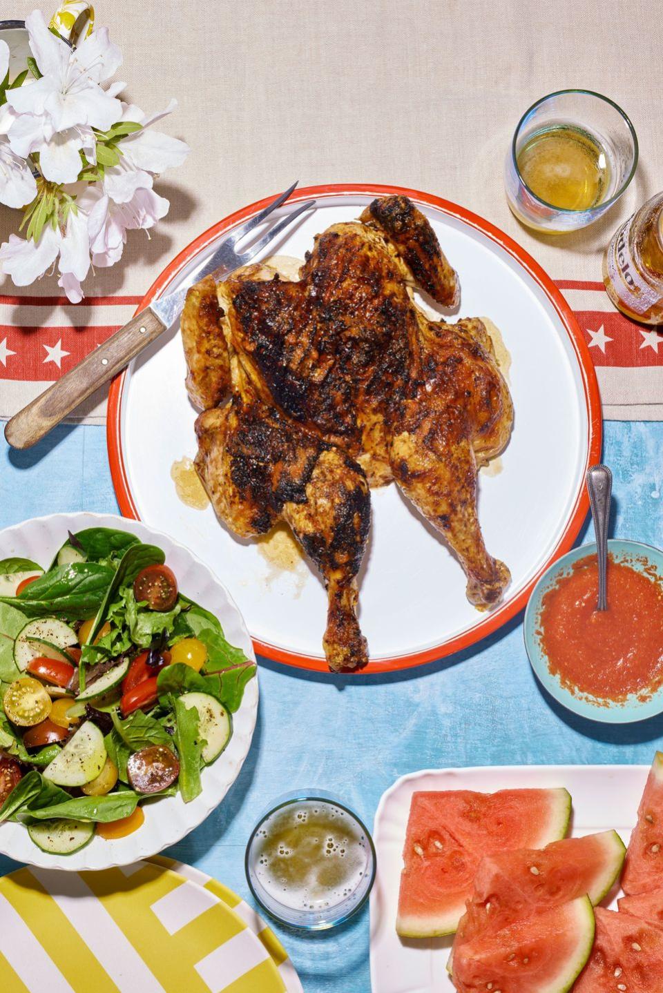 spatchcock chicken on a white round serving plate with a bowl of piri piri sauce to the side