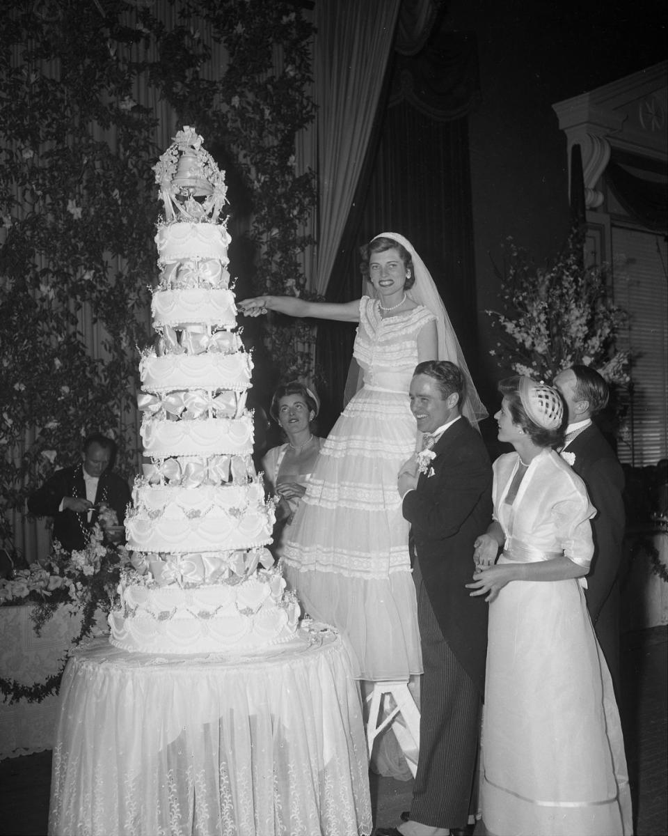 <p>Robert Sargent Shriver, Jr., steadies his bride, Eunice Kennedy, as she climbs onto a chair to cut the top of their wedding cake. The couple got in May 1953, a few months before her older brother, John F. Kennedy, tied the knot. </p>