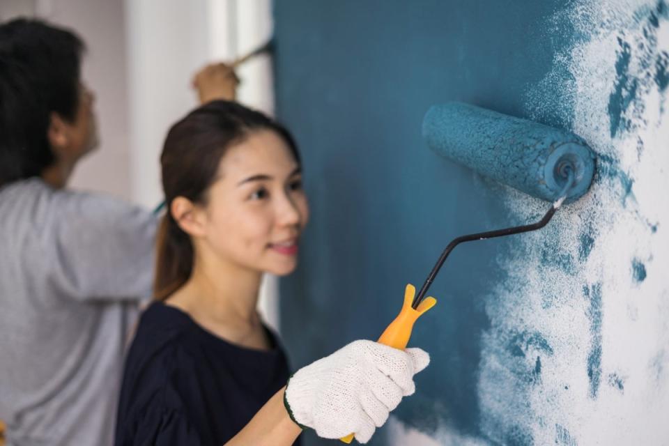 Woman painting wall blue using a paint roller. Man painting in background.