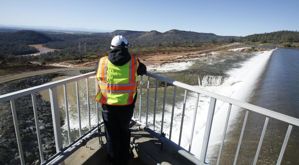 A employee of the Department of Water Resources watches as water flows over the emergency spillway at Oroville Dam Saturday, Feb. 11, 2017, in Oroville, Calif. Water started flowing over the spillway, at the nation's tallest dam, for the first time Saturday morning after erosion damaged the Northern California dam's main spillway.(AP Photo/Rich Pedroncelli)