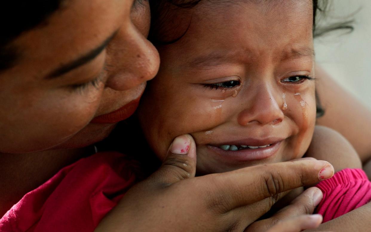 A migrant child's tears are wiped away by her mother as they receive medical care at a sidewalk clinic in refugee camp in Matamoros, Mexico - AP