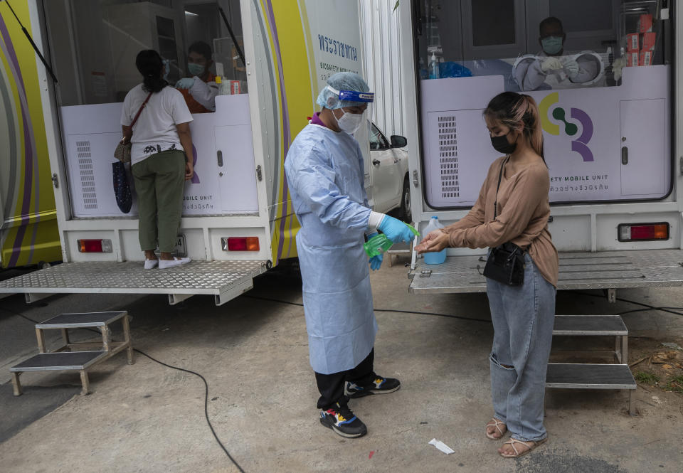 A health worker sprays disinfectant on hands after collecting a nasal swab from worker in a local entertainment venue area where a new cluster of COVID-19 infections were found in Bangkok, Thailand, Thursday, April 8, 2021. Thailand has confirmed its first local cases of the coronavirus variant first detected in the U.K., raising the likelihood that it is facing a new wave of the pandemic, a senior doctor said Wednesday. (AP Photo/Sakchai Lalit)