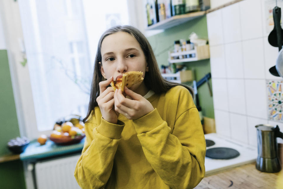 Close-up of tween eating slice of Pizza in Kitchen.