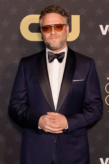 Man in a navy suit with a bow tie stands in front of event backdrop at the Critics' Choice Awards