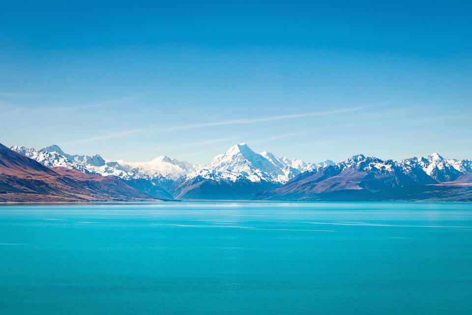 Beautiful turquoise Lake Tekapo under blue cloudless summer sky. The famous snow covered Aoraki Mount Cook in the background at the horizon. Lake Tekapo, Aoraki Mount Cook National Park, Caterbury, New Zealand.