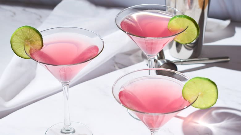 Three Cosmopolitan cocktails garnished with limes