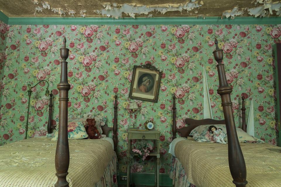 Two twin beds and floral wallpaper of an abandoned bedroom.
