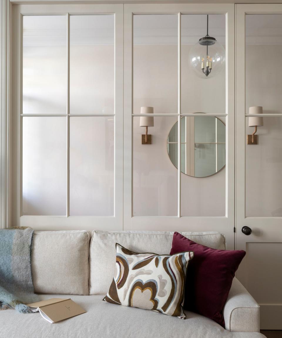 living room with cream sofa and glass doors behind to hallway with stained glass front door