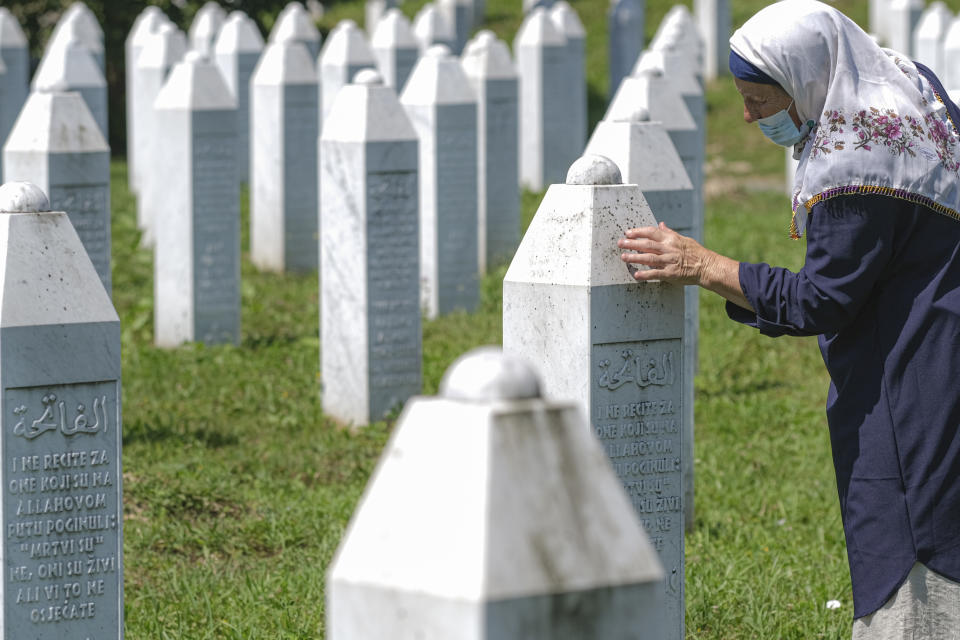 A woman touches a grave stone in Potocari, near Srebrenica, Bosnia, Saturday, July 11, 2020. Mourners converged on the eastern Bosnian town of Srebrenica for the 25th anniversary of the country's worst carnage during the 1992-95 war and the only crime in Europe since World War II that has been declared a genocide. (AP Photo/Kemal Softic)