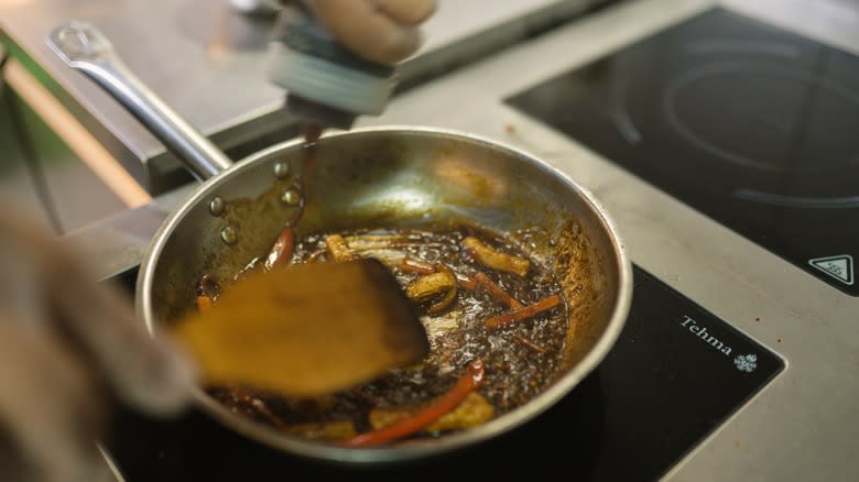 cook pouring soy sauce into wok