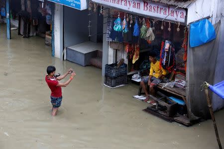 A man uses his mobile phone to take pictures of a shopkeeper at a waterlogged street after rainfall in Kolkata. REUTERS/Rupak De Chowdhuri