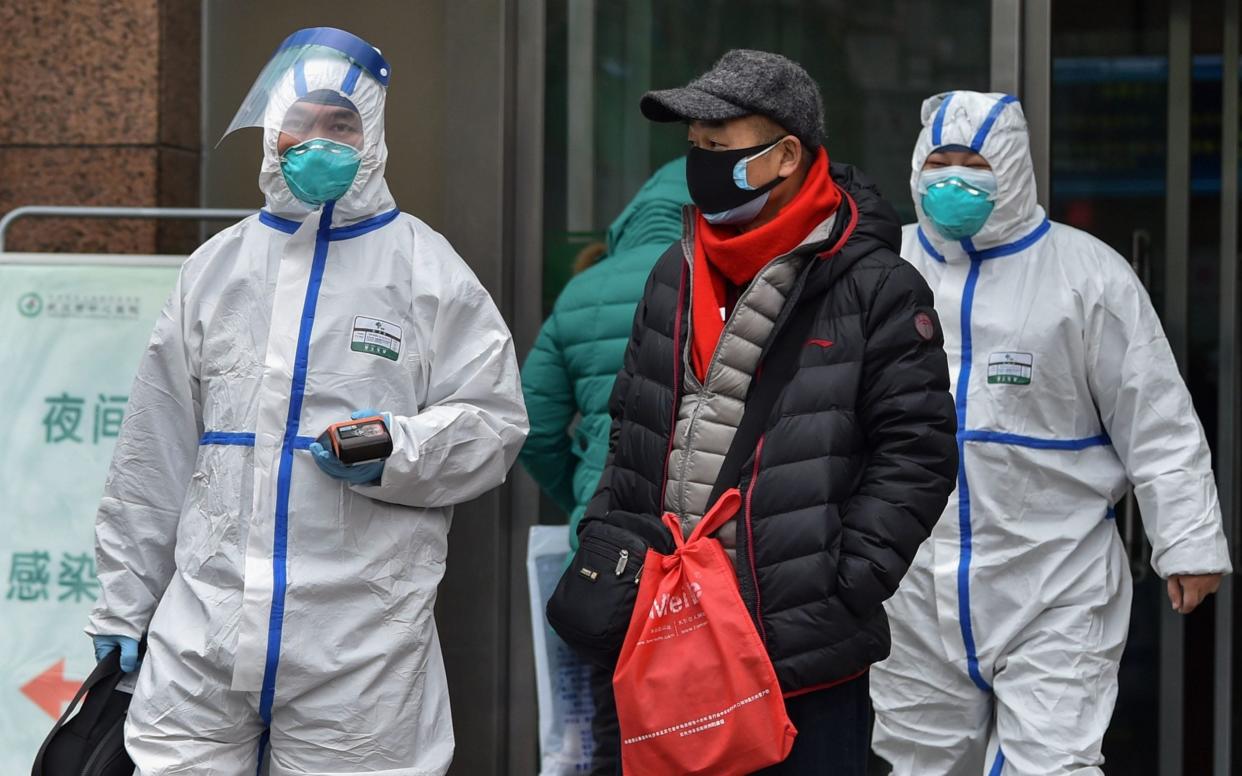 Medical staff wearing clothing to protect against a previously unknown virus walk outside a hospital in Wuhan - AFP