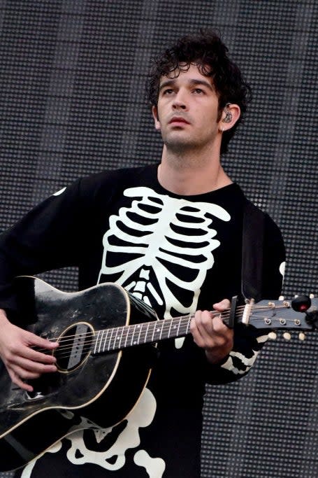 Person playing guitar, wearing a skeleton-print outfit, standing in front of a large screen