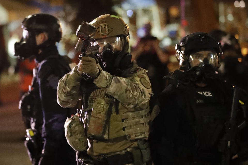 A federal officer points a non-lethal weapon at demonstrators during a Black Lives Matter protest at the Mark O. Hatfield United States Courthouse Thursday, July 30, 2020, in Portland, Ore. (AP Photo/Marcio Jose Sanchez)