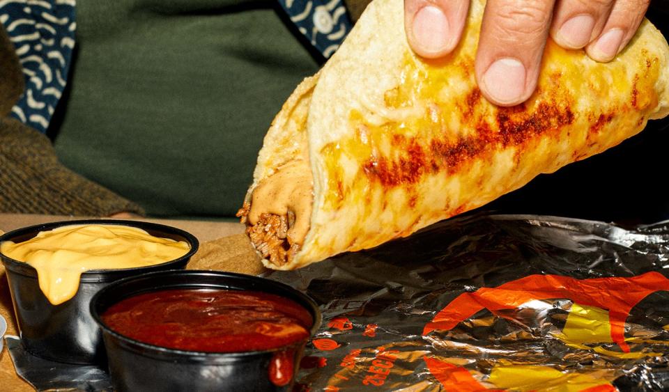A hand preparing to dip Taco Bell's Grilled Cheese Dipping Taco into a pot of red sauce and a pot of nacho-cheese sauce.