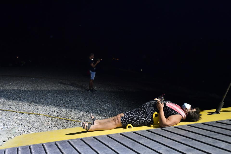 A woman lays in a docked ferry during a wildfire at Pefki village on Evia island, about 189 kilometers (118 miles) north of Athens, Greece, Sunday, Aug. 8, 2021. The fire in Evia, Greece's second-largest island, began Aug. 3 and has cut across the popular summer destination from coast to coast as it burned out of control. (AP Photo/Michael Varaklas)