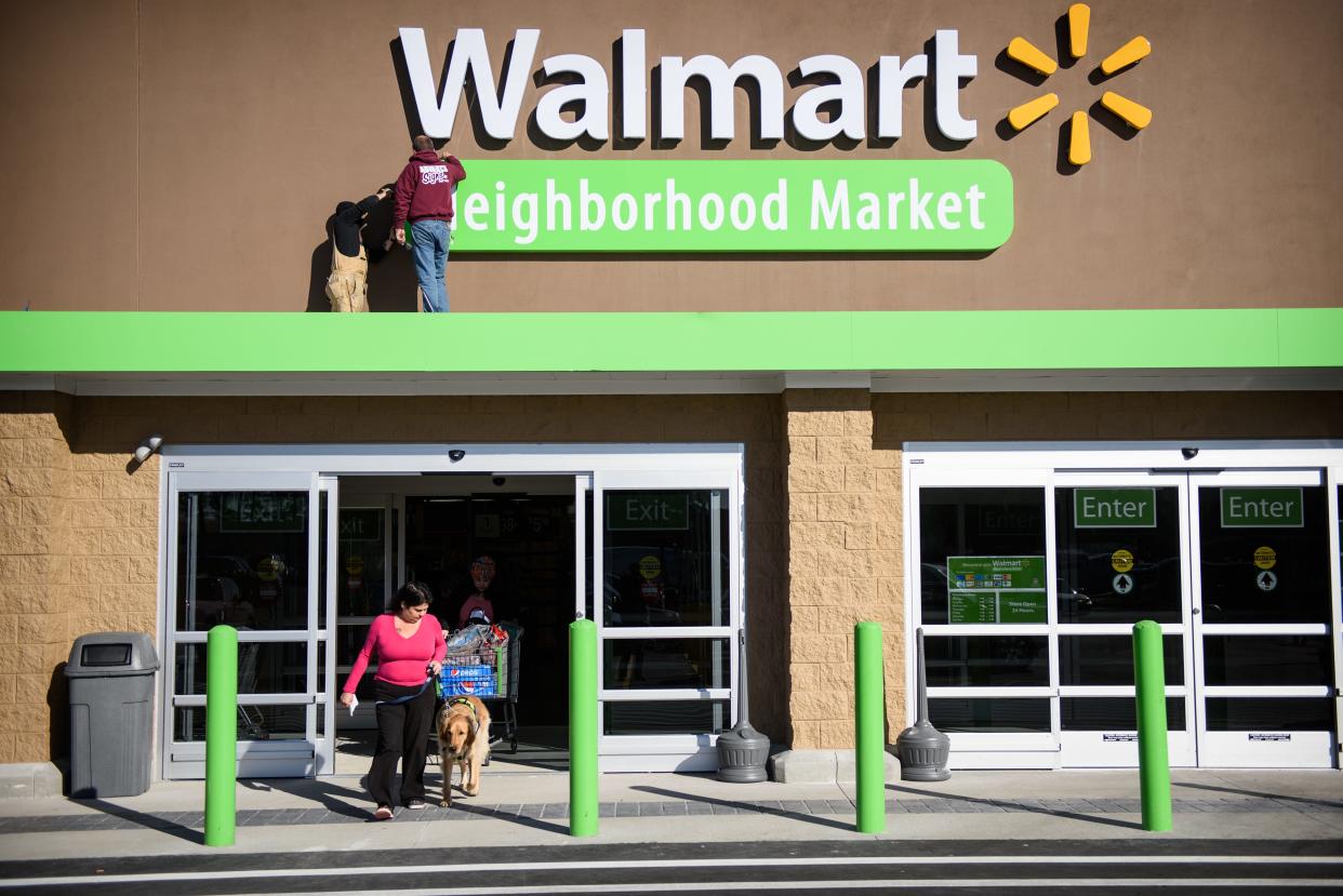 Workers work on the Walmart sign while shoppers come and go at the new Walmart Neighborhood Market on Raeford Road, Thursday, Jan. 8, 2015.