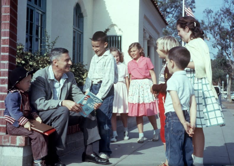 American author and illustrator Dr Seuss (Theodor Seuss Geisel, 1904 - 1991) sits outdoors talking with a group of children, holding a copy of his book, 'The Cat in the Hat', La Jolla, California, April 25, 1957. (Photo by Gene Lester/Getty Images)