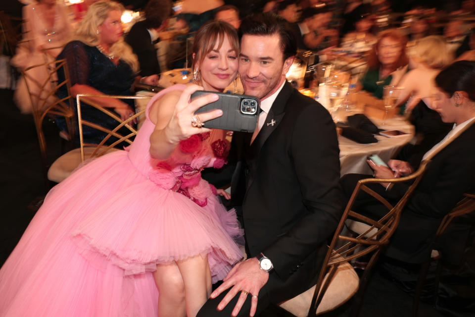 Kaley holds up her phone to take a selfie with Tom in the audience