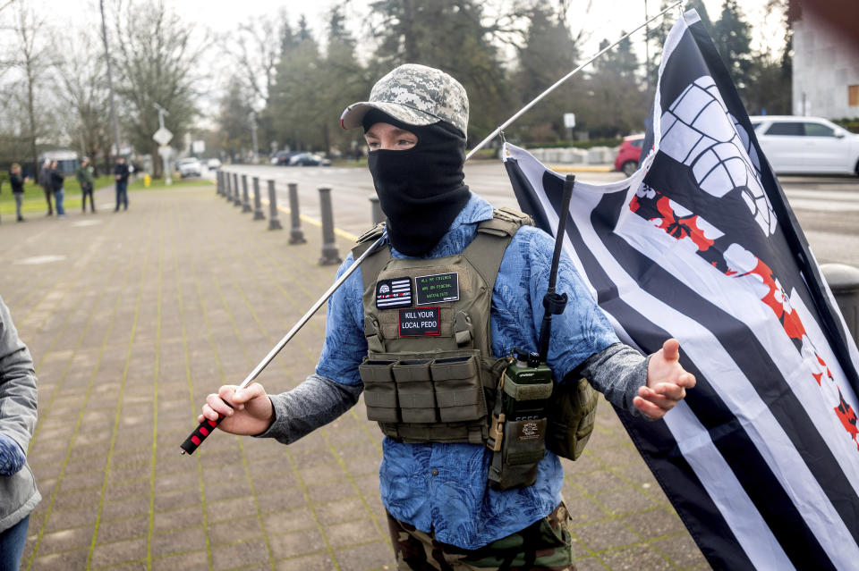 A protester who declined to give his name stands outside the Oregon State Capitol wearing a Hawaiian shirt and carrying a flag with a Hawaiian flower print on one stripe, both symbols associated with the boogaloo movement, on Sunday, Jan. 17, 2021, in Salem, Ore. People following the boogaloo movement, which promotes violence and a second U.S. civil war, have been showing up at protests across the nation armed and wearing tactical gear. But the anti-government movement has also adopted an unlikely public and online symbol: Hawaiian print shirts. (AP Photo/Noah Berger)