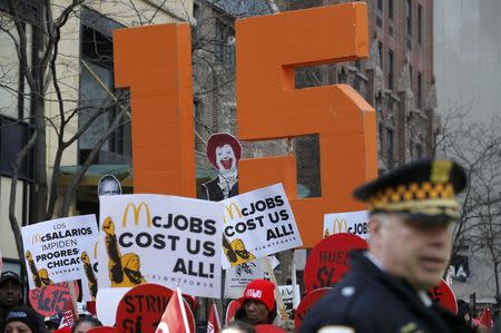 A Chicago Police officer looks on as demonstrators gather on the sidewalk with placards during a protest for a $15-an-hour nationwide minimum wage in downtown Chicago, Illinois, April 14, 2016. REUTERS/Jim Young