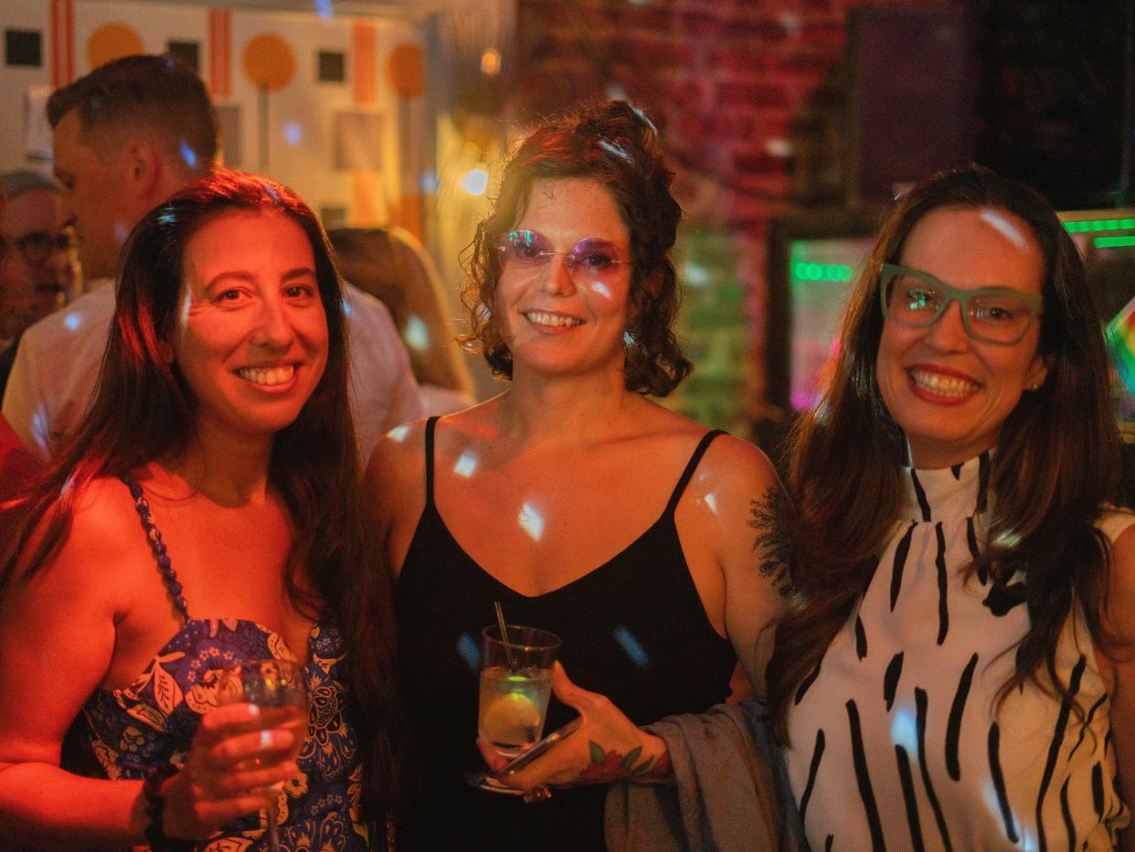 barbara corbellini duarte, violet augustine, and erica berenstein at the moving isa premiere. they're three women wearing dreses, smiling, and holding drinks amid party lights