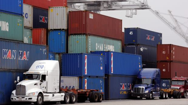 Trucks line up next to a wall of shipping containers four high waiting to be loaded at the Port of Long Beach.