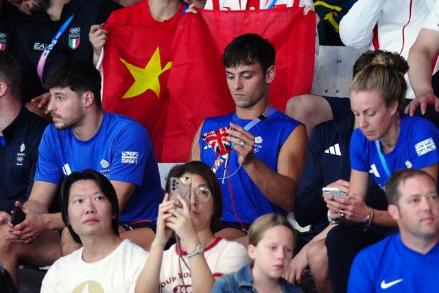 Tom Daley knitting as he sits in the stands watching Olympic diving action