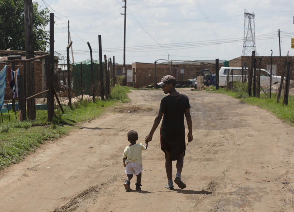 A woman and child walk down a dirt road in the Masakhane Township, near the coal-powered Duvha power station, near Emalahleni (formerly Witbank) east of Johannesburg, Thursday, Nov. 17, 2022. Living in the shadow of one of South Africa’s largest coal-fired power stations, residents of Masakhane fear job losses if the facility is closed as the country moves to cleaner energy. A significant polluter because it relies on coal to generate about 80% of its electricity, South Africa plans to reduce that to 59% by 2030 by phasing out some of its 15 coal-fired power stations and increasing its use of renewable energy. (AP Photo/Denis Farrell)