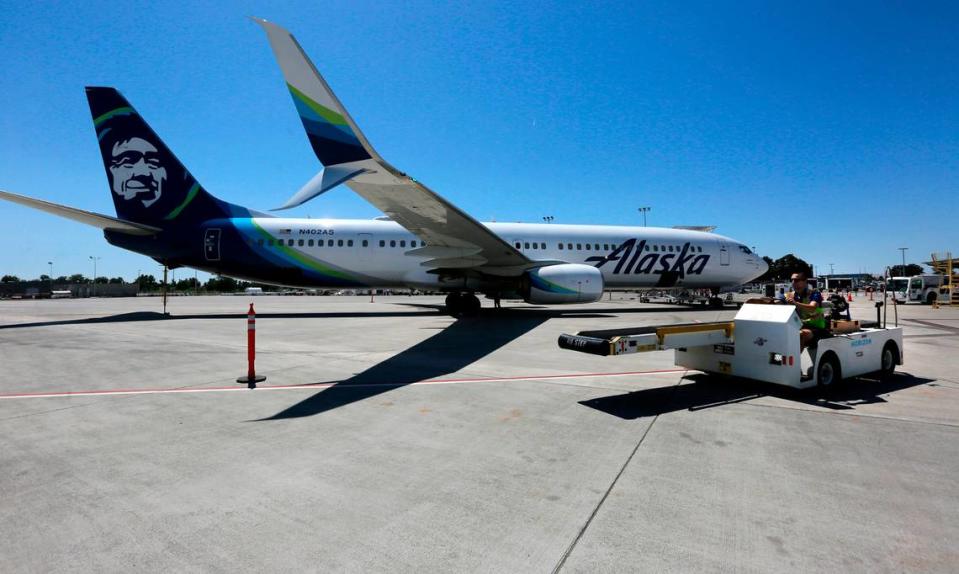 A baggage handler drives equipment past an Alaska Airline jet preparing to depart from the Tri-Cities Airport in Pasco.