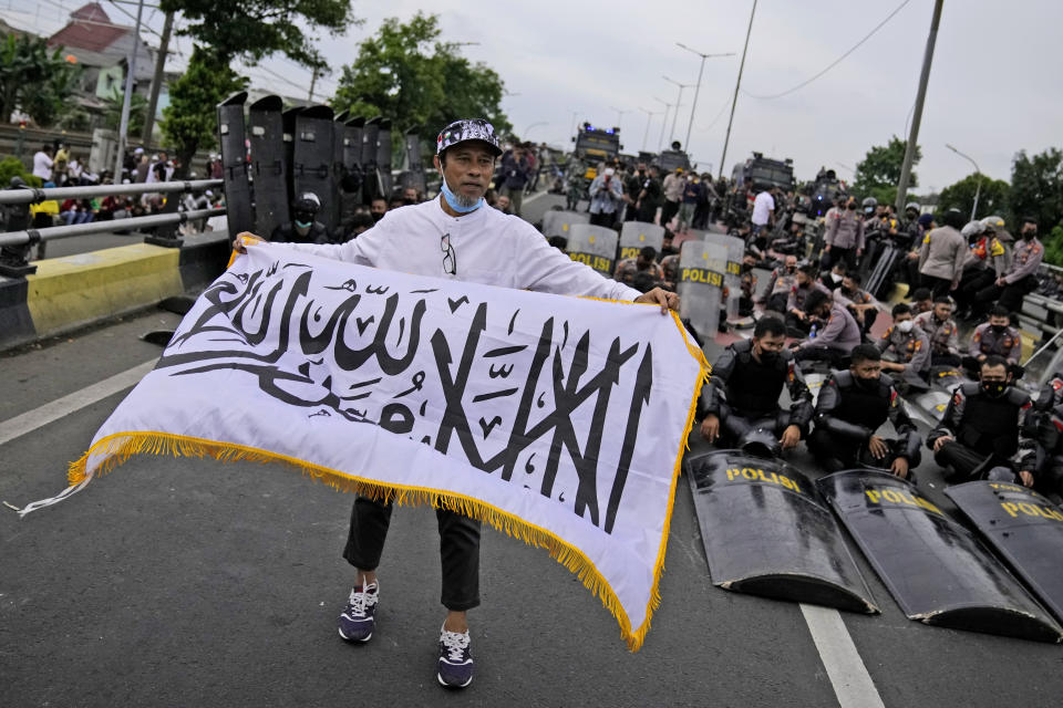 A supporter of firebrand cleric Rizieq Shihab displays a flag with Arabic writings that read "There's no God but Allah and Muhammad is His messenger", as police officers look on during a rally near the district court where his sentencing hearing is held in Jakarta, Indonesia, Thursday, June 24, 2021. The influential cleric was sentenced to another four years in prison on Thursday for concealing information about his coronavirus test result. (AP Photo/Dita Alangkara)