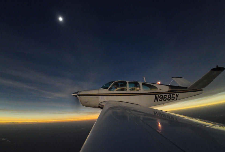 total solar eclipse in the top left part of the image photographed from the wing of a airplane which is in the center of the frame.