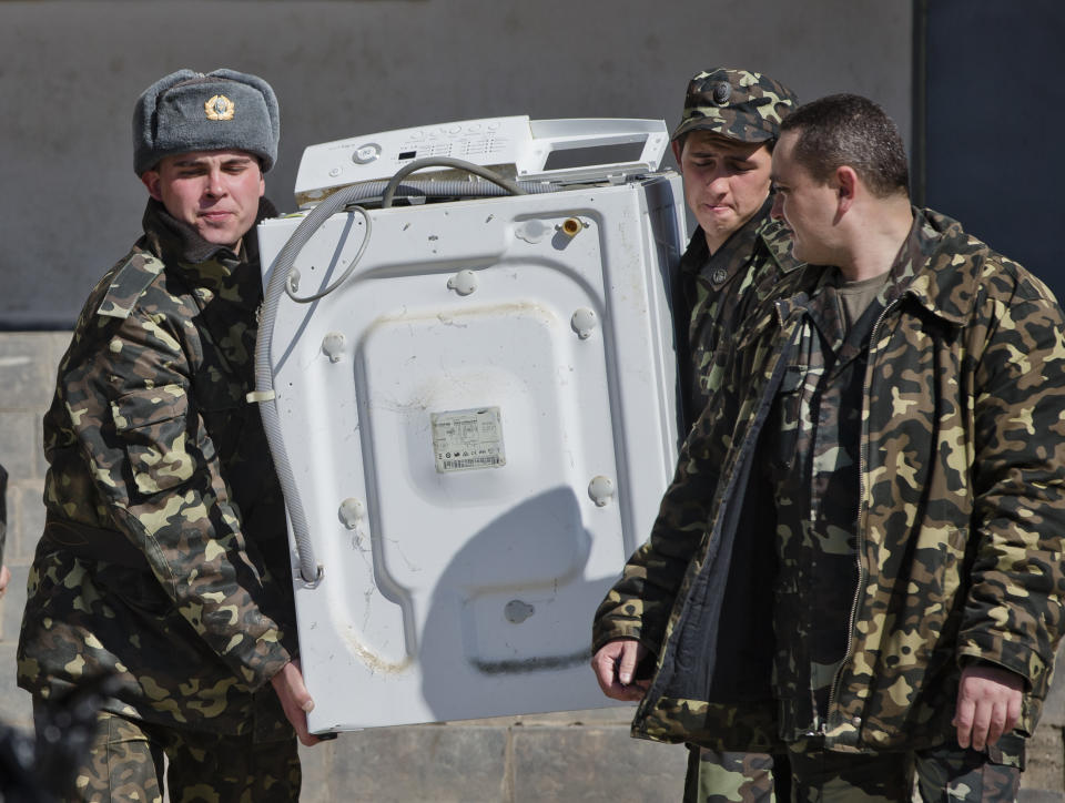 Ukrainian airmen carry a washing machine while removing their belongings from the Belbek air base, outside Sevastopol, Crimea, Friday, March 21, 2014. The base commander Col. Yuliy Mamchur said he was asked by the Russian military to turn over the base but is unwilling to do so until he receives orders from the Ukrainian defense ministry. (AP Photo/Vadim Ghirda)