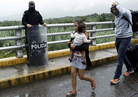 A woman carrying a child walks past a Colombian policeman after having crossed from Venezuela over the Simon Bolivar international bridge in Cucuta, Colombia February 13, 2018. REUTERS/Carlos Eduardo Ramirez