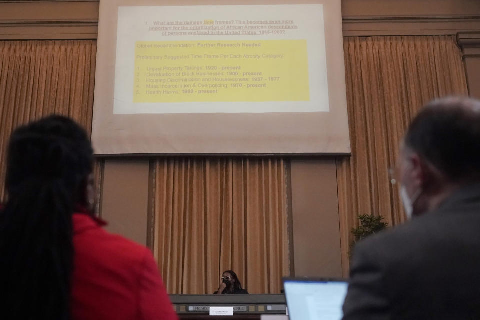 Task Force Chair Kamilah Moore, middle rear, speaks as research consultants Dr. Kaycea Campbell, foreground left, and Dr. Thomas Craemer, foreground right, listen during a meeting by the Task Force to Study and Develop Reparation Proposals for African Americans in Oakland, Calif., Wednesday, Dec. 14, 2022. (AP Photo/Jeff Chiu)