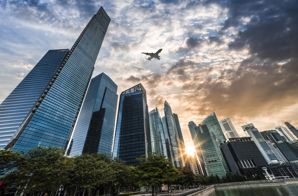 Airplane flying over the financial district in Singapore City at sunset, illustrating a story on the Forbes World's Billionaires List. 