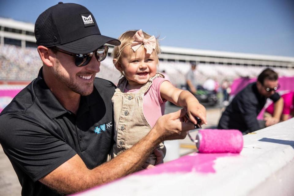 Daniel Hemric, left, holds his daughter, Rhen, while she paints during the Paint Pit Wall Pink event at the Charlotte Motor Speedway in Charlotte, N.C., on Tuesday, September 28, 2021.