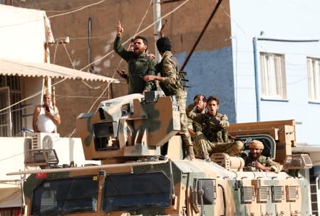 Members of Syrian National Army, known as Free Syrian Army, react as they drive on top of an armored vehicle in the Turkish border town of Ceylanpinar