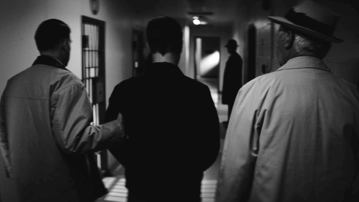  A black-and-white dramatization of Ed Gein being walked through a hallway in Psycho: The Lost Tapes of Ed Gein 