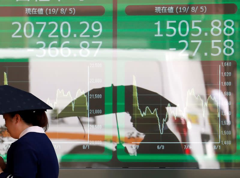 A woman walks past in front of an electric screen showing Japan's Nikkei share average outside a brokerage in Tokyo