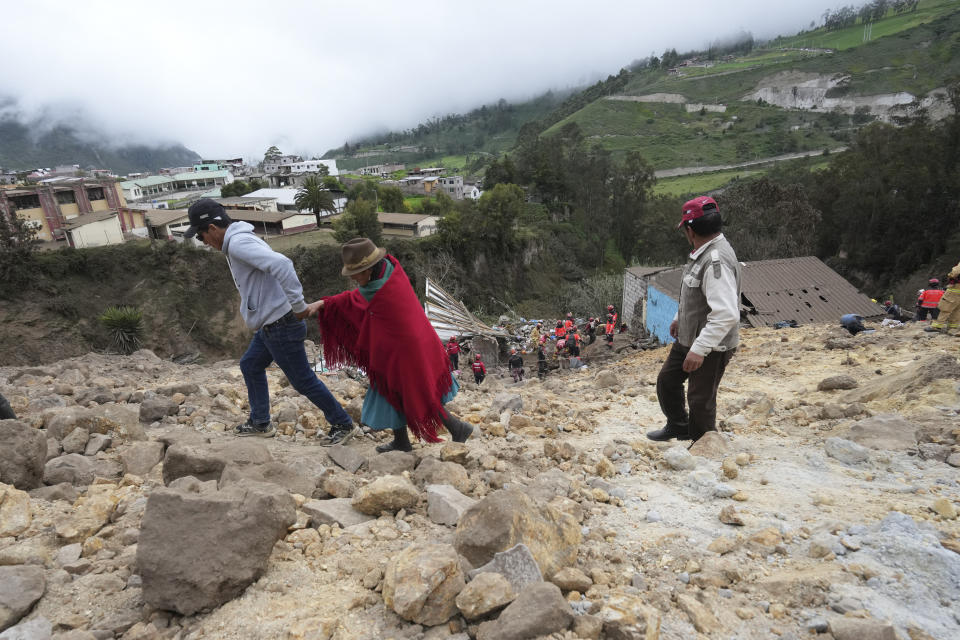 Residents walk on mud and stones after a deadly landslide buried dozens of homes in Alausi, Ecuador, Monday, March 27, 2023. (AP Photo/Dolores Ochoa)