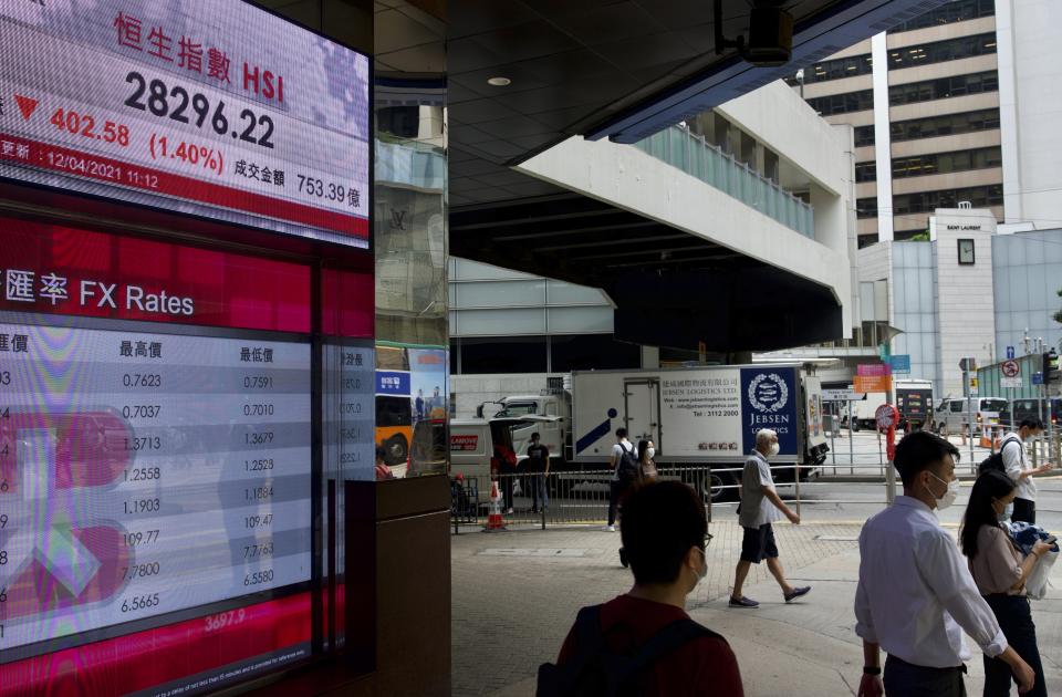 People walk past a bank's electronic board showing the Hong Kong share index at Hong Kong Stock Exchange in Hong Kong Monday, April 12, 2021. Asian shares were lower on Monday, as investors grew wary over the recent surge in coronavirus cases in many places while vaccinations are making scant headway. (AP Photo/Vincent Yu)