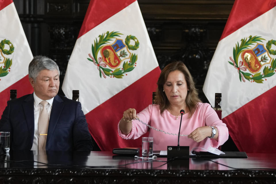 FILE - Peruvian President Dina Boluarte shows her necklace, accompanied by her lawyer Mateo Castaneda, during a press conference amid an investigation into whether she illegally received cash, luxury watches and jewelry, at the government palace in Lima, Peru, April 5, 2024. Prosecutors arrested Boluarte's brother, Nicanor Boluarte, and lawyer Castaneda, on Friday, May 10, 2024, for allegedly being part of a group that trafficked influence by appointing officials in exchange for money and forcing them to collect signatures to register a political party. (AP Photo/Martin Mejia, File)