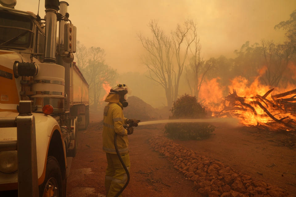 In this photo provided by Department of Fire and Emergency Services, a firefighter attends to a fire near Wooroloo, northeast of Perth, Australia, Tuesday, Feb. 2, 2021. An out-of-control wildfire burning northeast of the Australian west coast city of Perth has destroyed dozens of homes and was threatening more. (Evan Collis/DFES via AP)